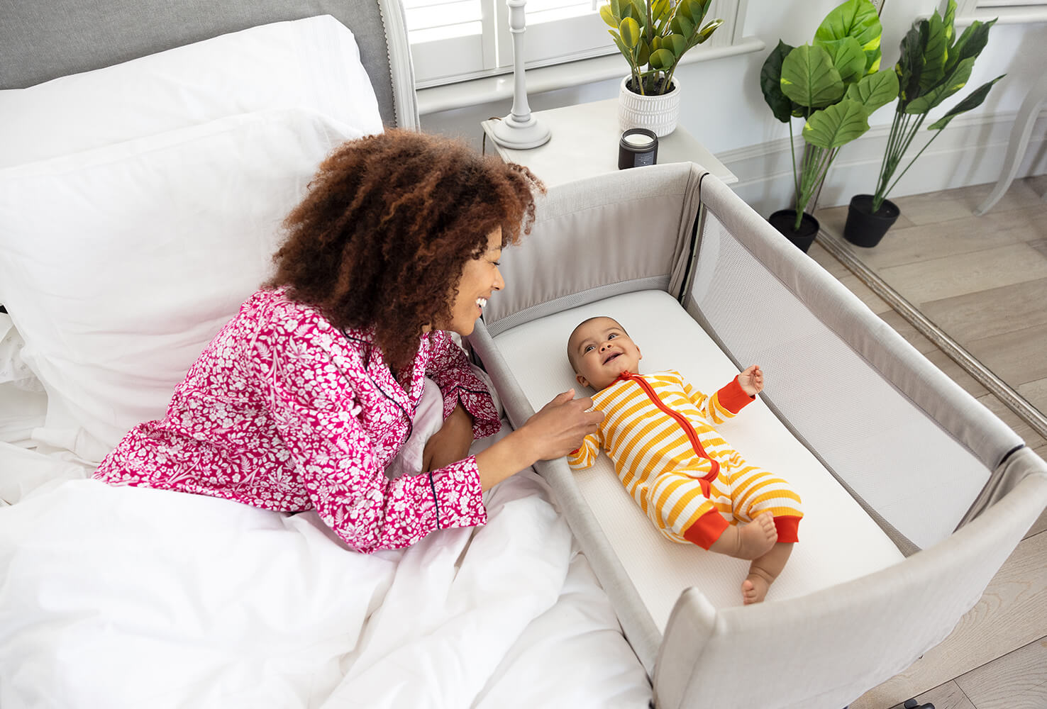 Mère allongée dans son lit et interagissant avec son bébé allongé dans le lit d’appoint de voyage Roomie Go.
