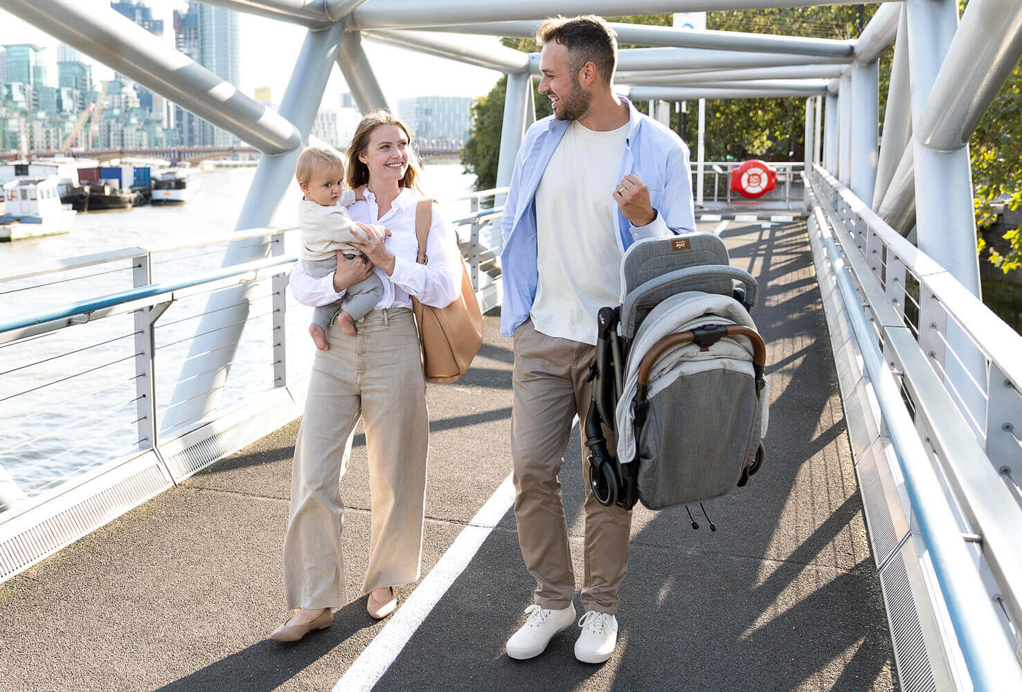   Joie tourist stroller folded being carried by dad while mom and baby walk by his side over a bridge.