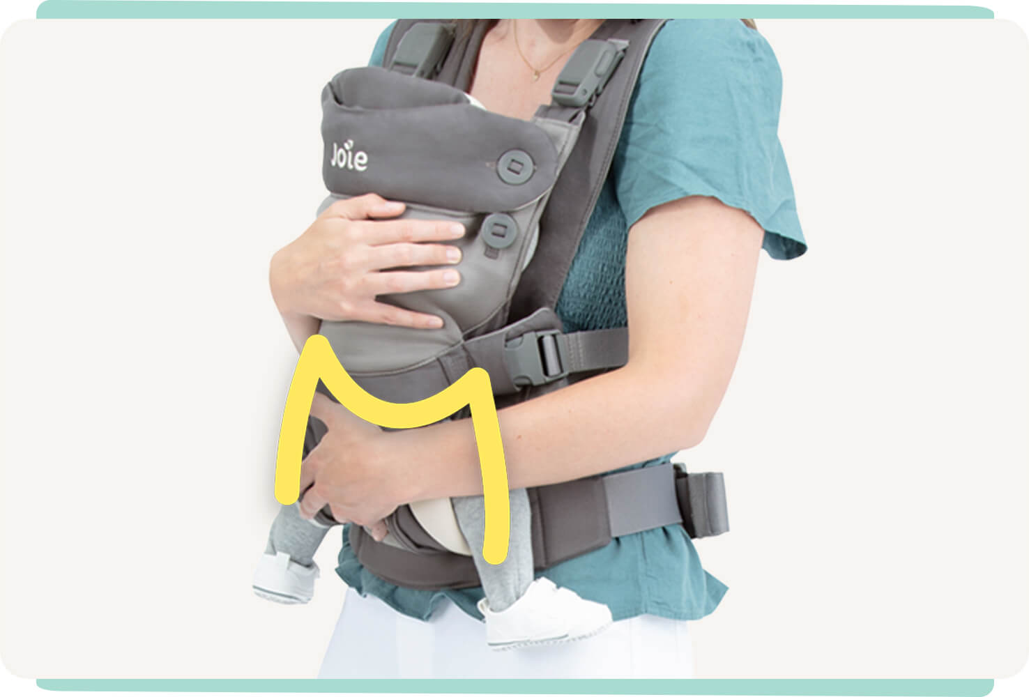 Closeup of a baby in a gray Joie Savvy Lite 3in1 baby carrier with a yellow line indicating the M shape of the baby’s hips