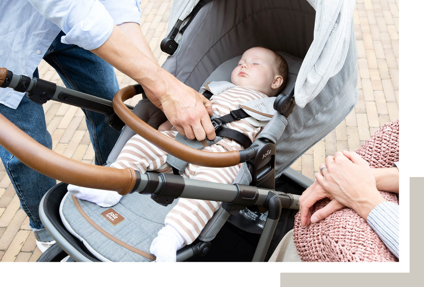 Gros plan sur un bébé endormi dans un landau Joie aeria, coloris gris clair, avec maman et papa à proximité.