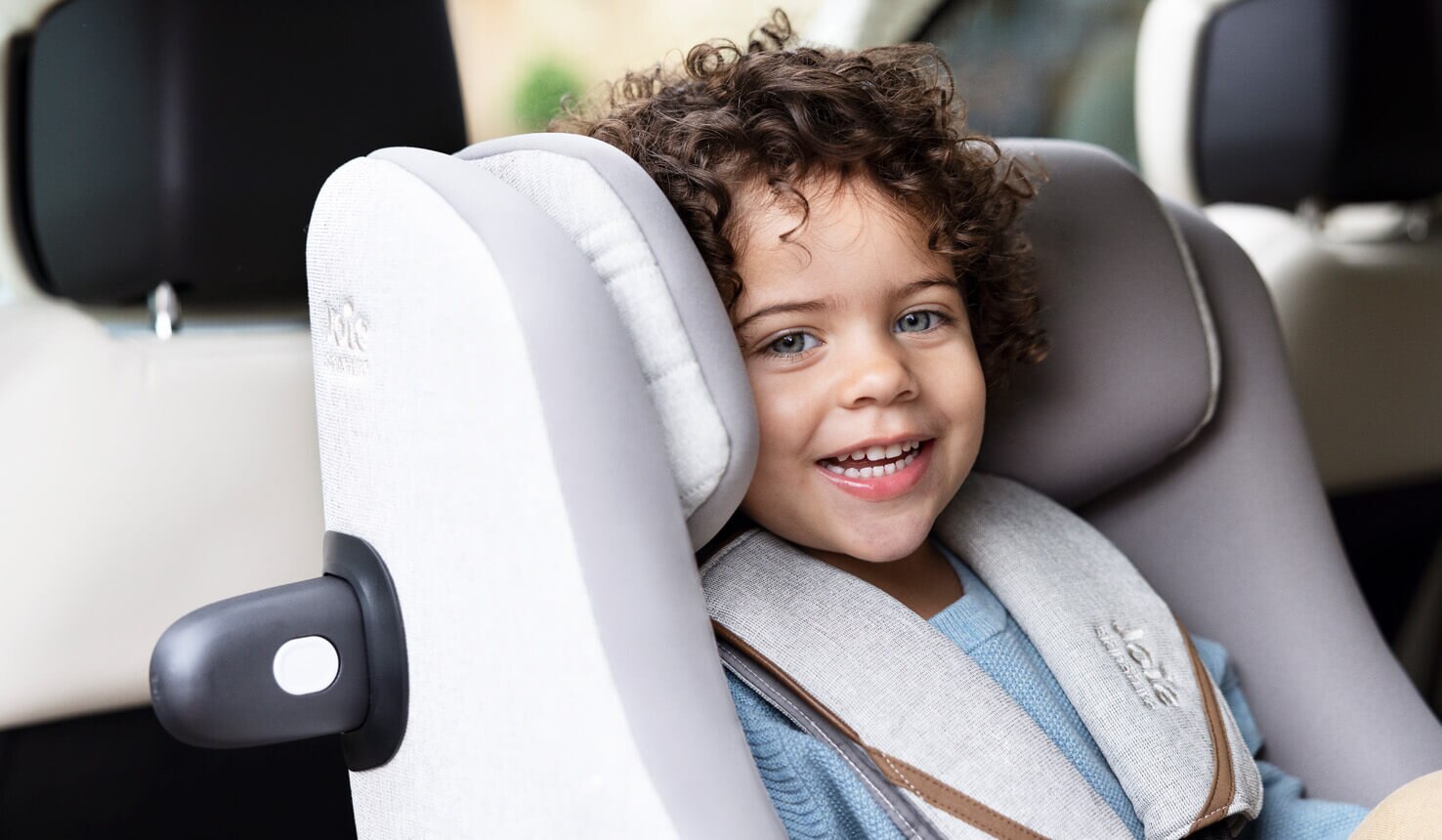 Close up of young boy smiling in a gray Joie i-Harbour car seat. 