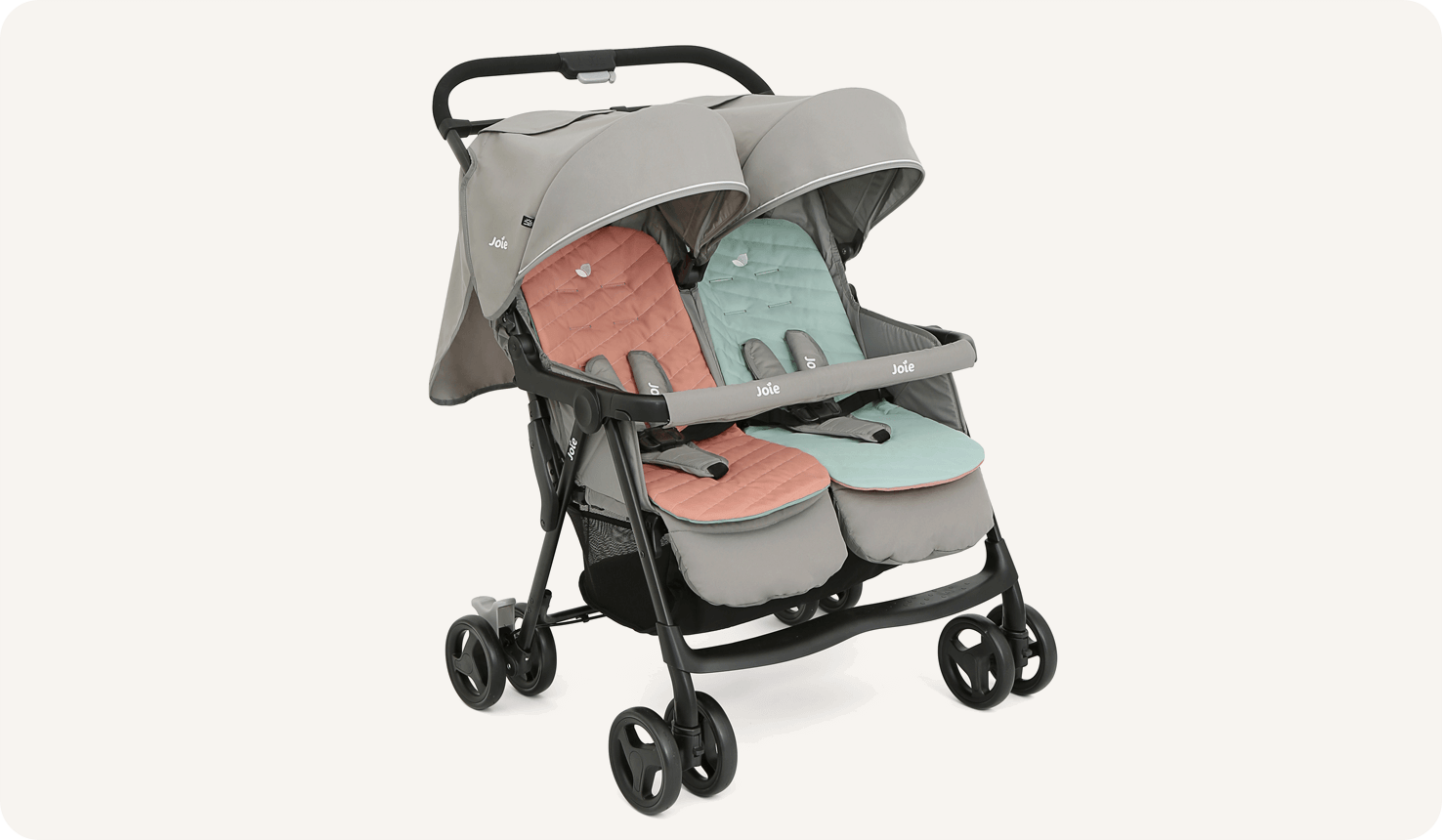   The Joie Aire Twin side-by-side double stroller in light gray at an angle, with a peach coloured seat insert on the left seat and a light blue insert on the right seat.