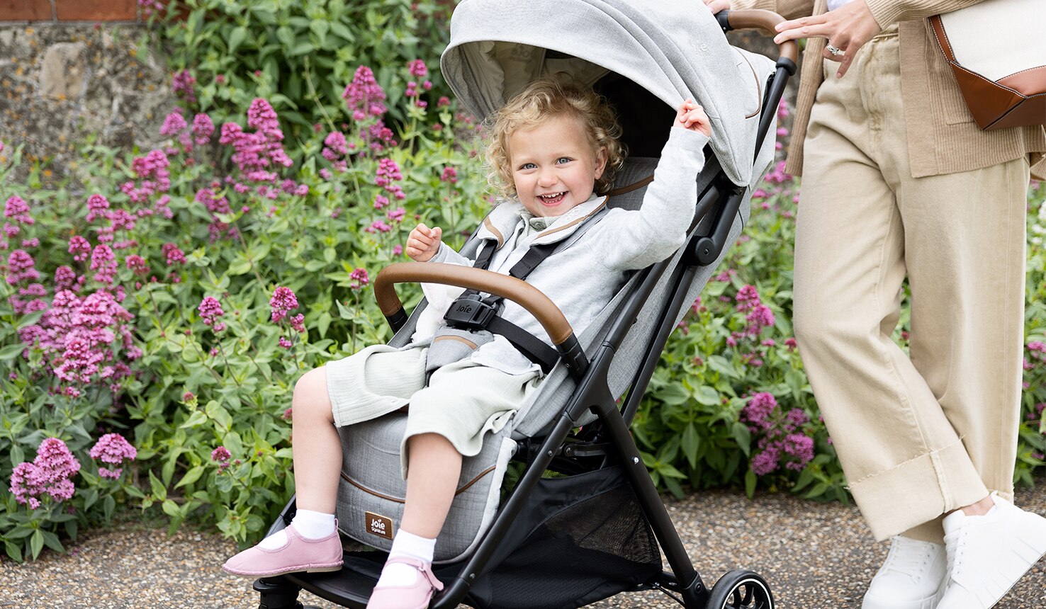 A blonde girl sitting in the Joie Parcel pushchair and smiling