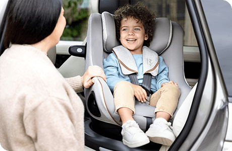 Une maman fait tourner un enfant plus âgé en position face à la route dans un siège auto Joie i-Harbour.