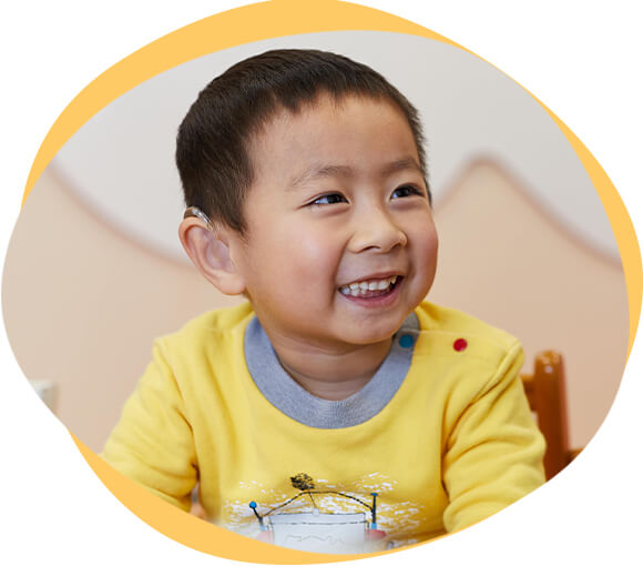 Smiling toddler wearing a hearing aid.
