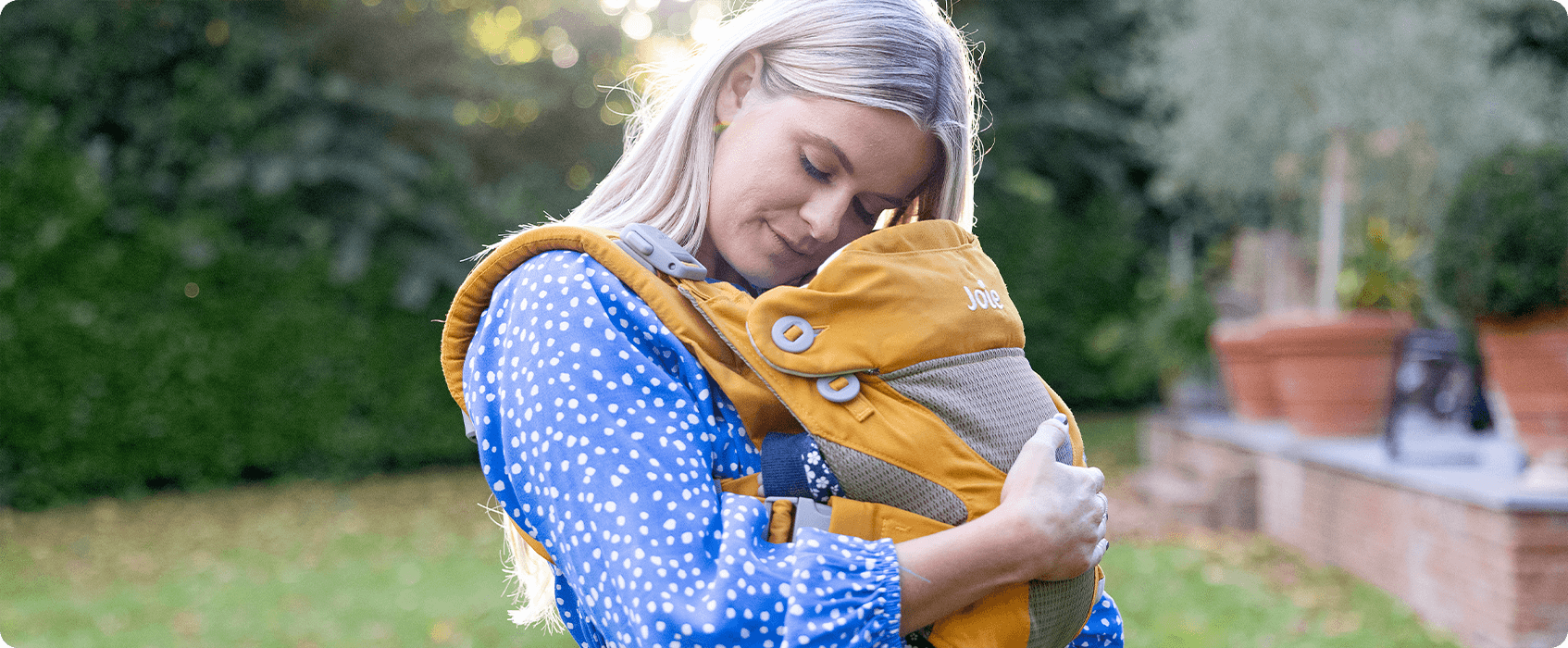 Mum cuddling baby in a mustard yellow Joie Savvy baby carrier